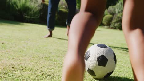 Midsection-of-african-american-father-and-son-playing-soccer-in-garden,-in-slow-motion