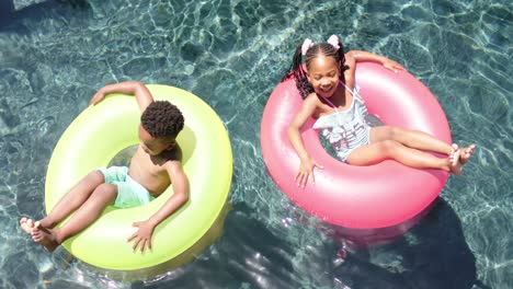 Happy-african-american-siblings-with-inflatables-at-pool,-in-slow-motion