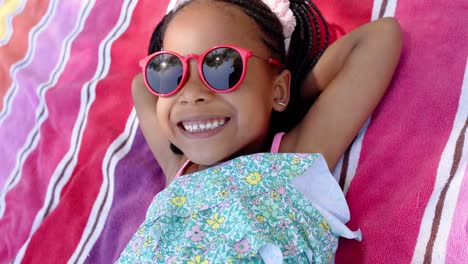 Fröhliches-Afroamerikanisches-Mädchen-Mit-Sonnenbrille,-Das-Auf-Einem-Handtuch-Liegt,-In-Zeitlupe