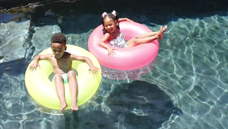 Glückliche-Afroamerikanische-Geschwister-Mit-Schlauchbooten-Am-Pool,-In-Zeitlupe