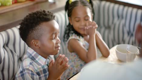 Happy-african-american-family-praying-before-breakfast,-in-slow-motion