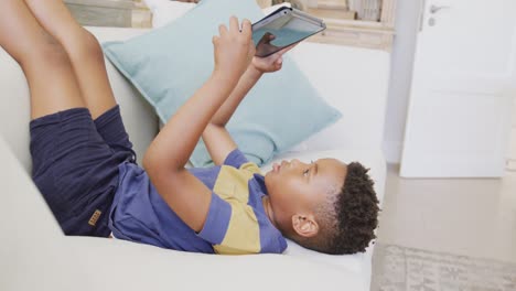 Happy-african-american-boy-sitting-on-sofa-and-using-tablet,-in-slow-motion
