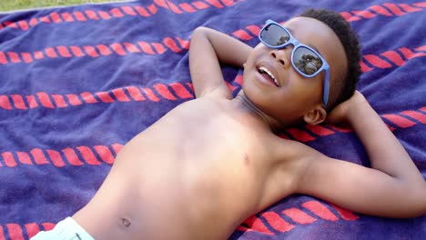 Happy-african-american-boy-with-sunglasses-lying-on-towel,-in-slow-motion