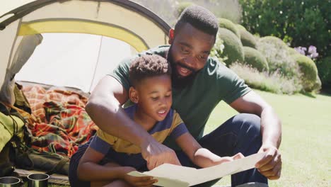 Glücklicher-Afroamerikanischer-Vater-Und-Sohn-Sitzen-Im-Zelt-Und-Lesen,-In-Zeitlupe