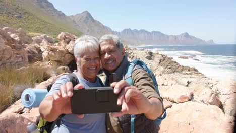 Happy-senior-biracial-couple-in-mountains-taking-selfie-with-smartphone,-in-slow-motion