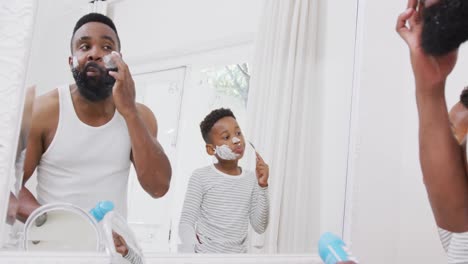 Happy-african-american-father-and-son-applying-shaving-cream-on-face-in-bathroom,-in-slow-motion