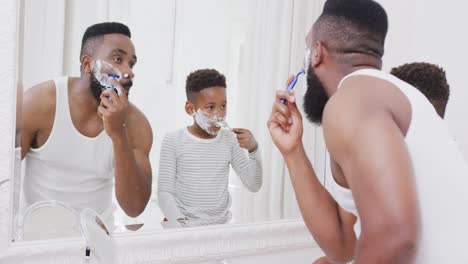 Happy-african-american-father-and-son-shaving-beard-in-bathroom,-in-slow-motion