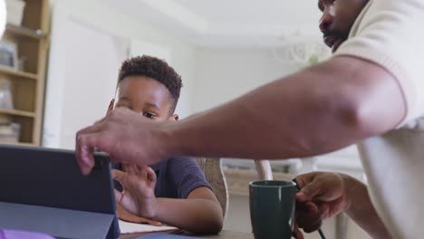 Happy-african-american-father-and-son-sitting-at-table-and-doing-homework-together,-in-slow-motion