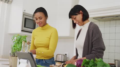 Happy-biracial-sisters-cooking-dinner-together-in-kitchen,-in-slow-motion