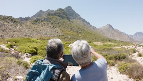Senior-biracial-couple-in-mountains-using-tablet,-in-slow-motion