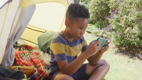 Glücklicher-Afroamerikanischer-Junge,-Der-Sein-Smartphone-Im-Zelt-Benutzt,-In-Zeitlupe
