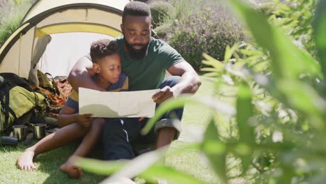Happy-african-american-father-and-son-sitting-in-tent-and-reading,-in-slow-motion