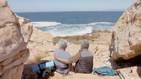 Happy-senior-biracial-couple-in-mountains-embracing-at-sea,-in-slow-motion