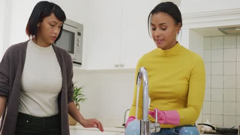Happy-biracial-sisters-cleaning-in-kitchen,-in-slow-motion