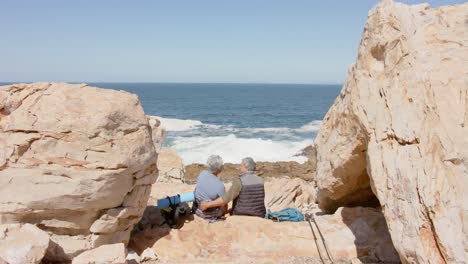 Happy-senior-biracial-couple-in-mountains-resting-at-sea,-in-slow-motion
