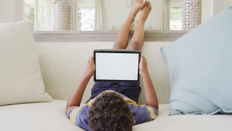 Happy-african-american-boy-sitting-on-sofa-and-using-tablet-with-copy-space,-in-slow-motion