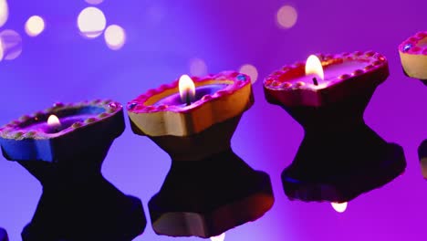 Close-up-of-burning-colourful-candles-celebrating-diwali-on-purple-background