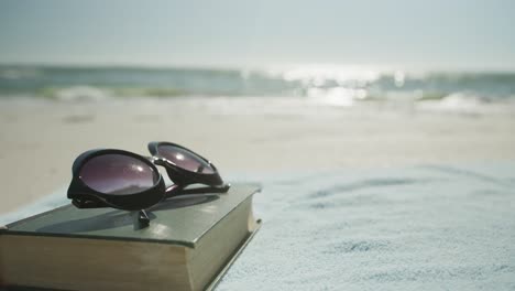 Nahaufnahme-Von-Buch,-Sonnenbrille-Und-Handtuch-Am-Strand,-In-Zeitlupe,-Mit-Kopierraum