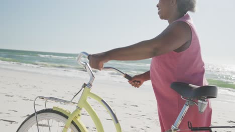 Glückliche-ältere-Afroamerikanische-Frau,-Die-Mit-Dem-Fahrrad-Am-Strand-Läuft,-In-Zeitlupe