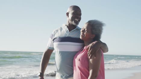 Glückliches-älteres-Afroamerikanisches-Paar,-Das-Am-Strand-Spaziert-Und-Sich-Umarmt,-In-Zeitlupe