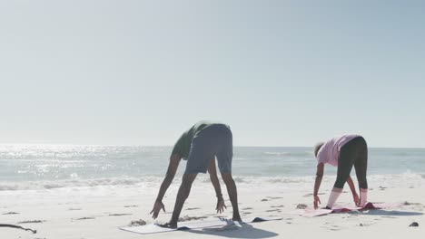 Glückliches-älteres-Afroamerikanisches-Paar,-Das-Yoga-Macht-Und-Sich-Am-Strand-Dehnt,-In-Zeitlupe
