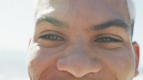 Portrait-of-happy-biracial-man-smiling-at-beach,-in-slow-motion