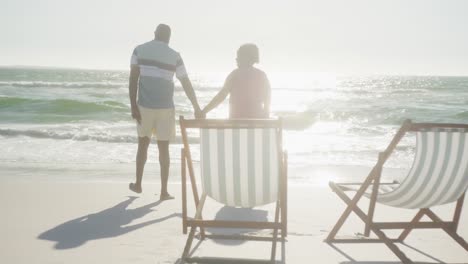 Happy-senior-african-american-couple-walking-and-holding-hands-at-beach,-in-slow-motion