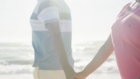 Happy-senior-african-american-couple-walking-and-holding-hands-at-beach,-in-slow-motion