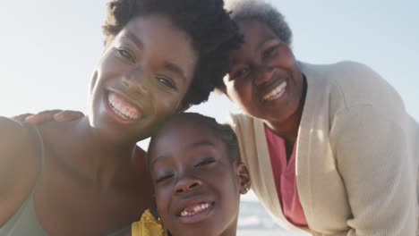 Portrait-of-happy-african-american-grandmother,-mother-and-daughter-smiling-at-beach,-in-slow-motion