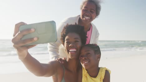 Happy-african-american-grandmother,-mother-and-daughter-taking-selfie-at-beach,-in-slow-motion