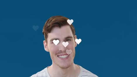 Animation-of-heart-shapes-flying-over-portrait-of-caucasian-young-man-smiling-over-blue-background