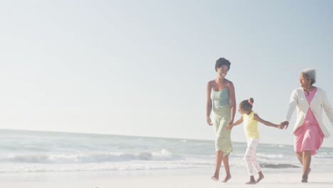 Happy-african-american-grandmother,-mother-and-daughter-walking-at-beach,-in-slow-motion,-copy-space