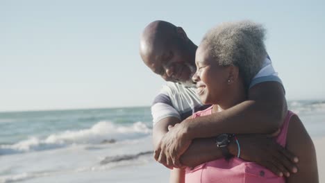 Happy-senior-african-american-couple-embracing-at-beach,-in-slow-motion
