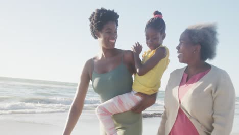 Glückliche-Afroamerikanische-Großmutter,-Mutter-Und-Tochter,-Die-In-Zeitlupe-Am-Strand-Spazieren-Gehen