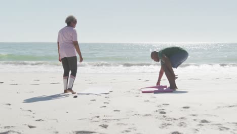 Happy-senior-african-american-couple-placing-yoga-mats-at-beach,-in-slow-motion