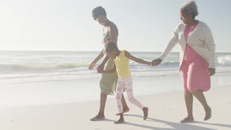 Happy-african-american-grandmother,-mother-and-daughter-walking-at-beach,-in-slow-motion