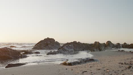 Beach-landscape-with-sea,-rocks-and-blue-sky-at-sundown,-in-slow-motion