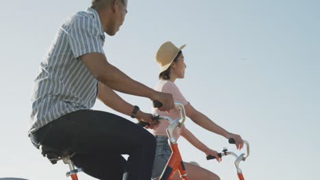 Happy-biracial-couple-riding-bikes-on-promenade,-in-slow-motion