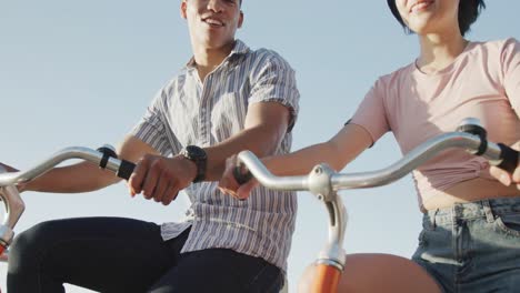 Happy-biracial-couple-riding-bikes-on-promenade,-in-slow-motion
