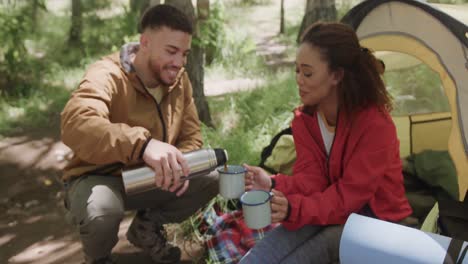 Happy-african-american-couple-camping,-drinking-coffee-in-forest,-slow-motion