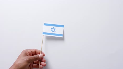Close-up-of-hand-holding-flag-of-israel-on-white-background-with-copy-space