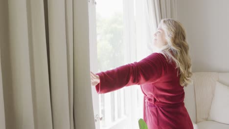 Happy-caucasian-plus-size-woman-uncovering-windows-with-curtain-in-slow-motion