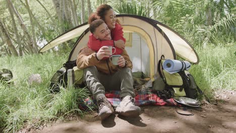 Happy-african-american-couple-camping,-drinking-coffee-and-embracing-in-forest,-slow-motion