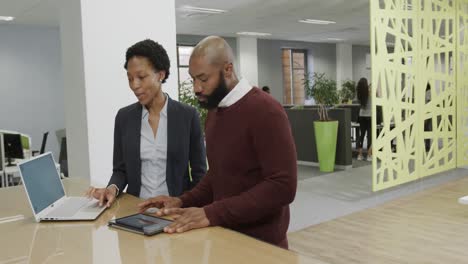 African-american-business-people-discussing-work-and-using-laptop-in-office-in-slow-motion