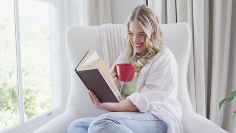 Portrait-of-happy-caucasian-plus-size-woman-reading-book-and-drinking-coffee
