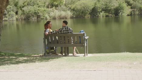 Happy-african-american-couple-sitting-on-bench-at-lake-in-forest,-slow-motion