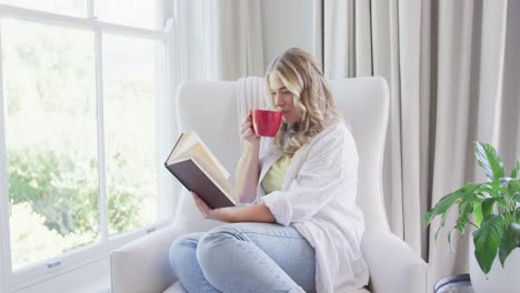 Portrait-of-happy-caucasian-plus-size-woman-reading-book-and-drinking-coffee-in-slow-motion