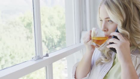 Happy-caucasian-plus-size-woman-talking-on-smartphone-and-drinking-tea-in-slow-motion