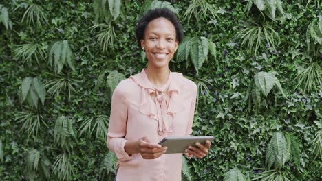 Portrait-of-happy-african-american-businesswoman-using-tablet-and-smiling-in-garden,-in-slow-motion