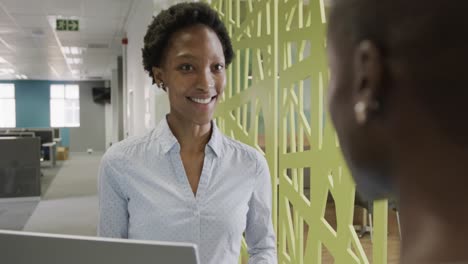 Two-african-american-businesswomen-discussing-work-and-using-laptop-in-office-in-slow-motion